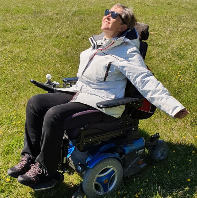 En lycklig Lise i sin elrullstol, i solen på en grön gräsmatta.
